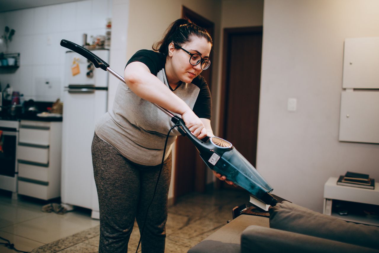 Crafting Captivating Headlines: Your awesome post title goes here A woman vacuuming a couch in a cozy living room setting, emphasizing daily housework.